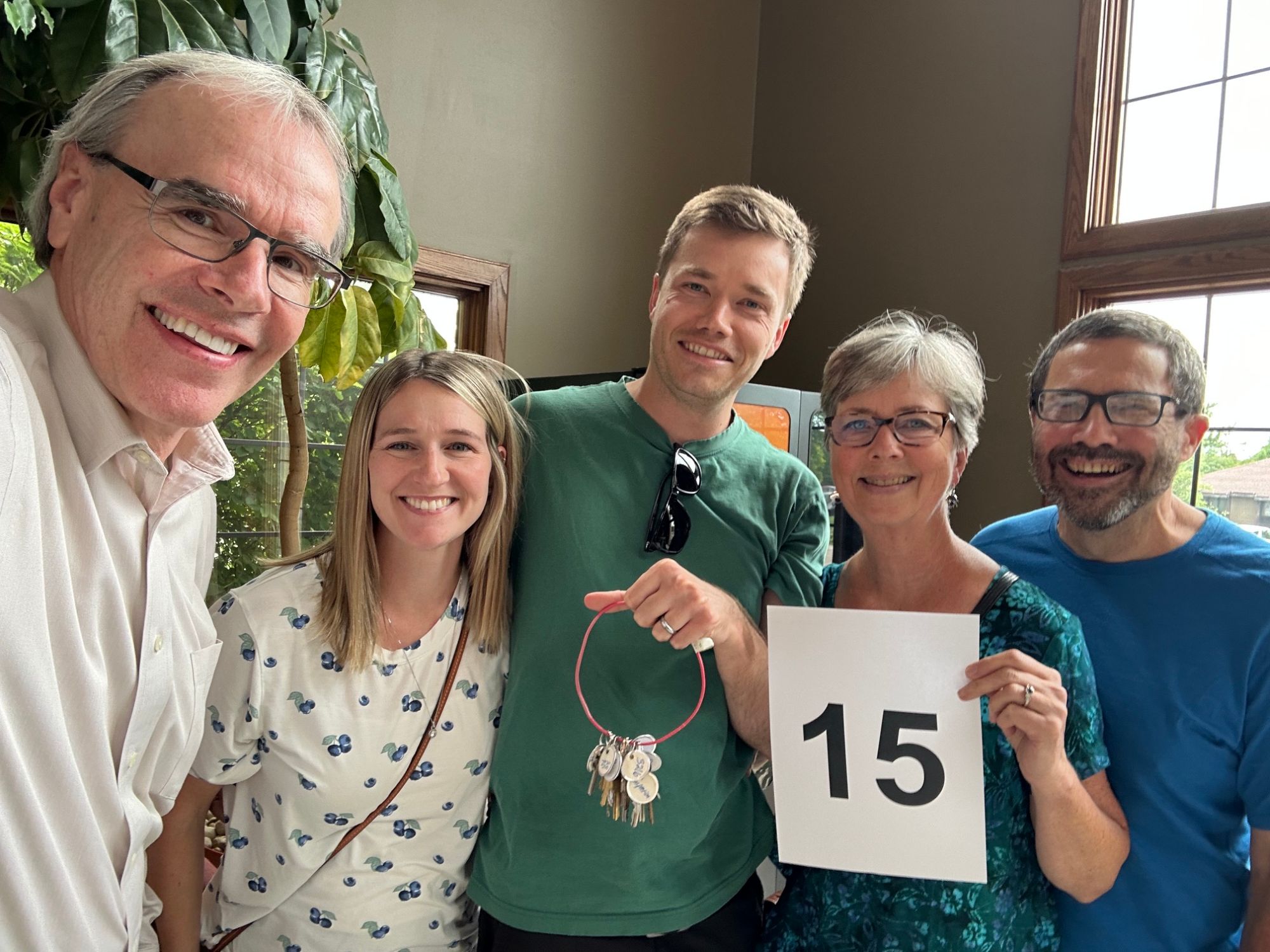 Nate, Liz and Charlotte all stand next to David Campbell, realtor, smiling as they face towards the camera. Nate is holding a ring of house keys.