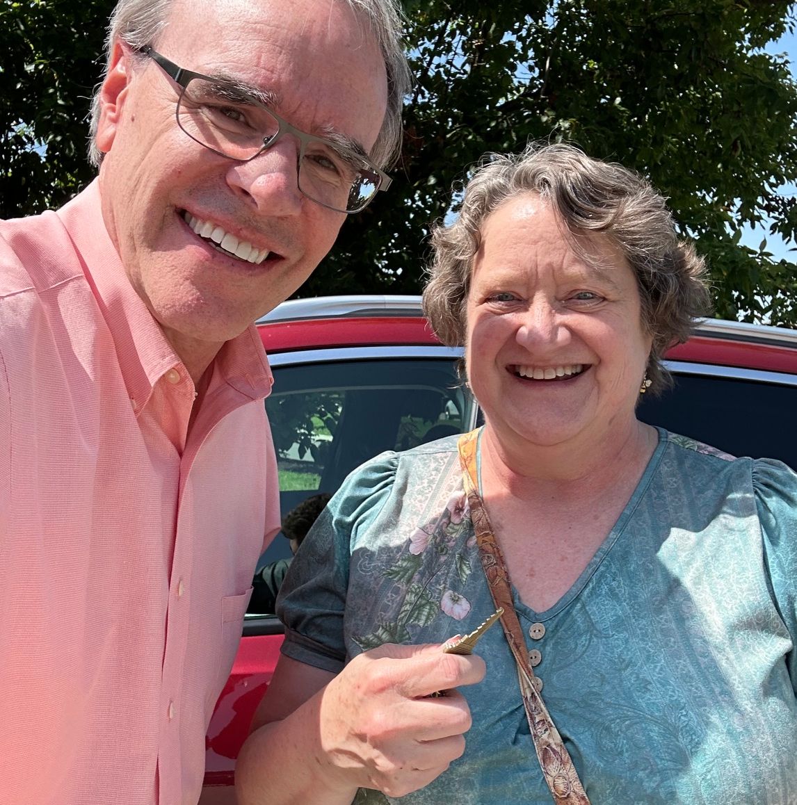 Deb stands next to David Campbell, realtor, holding a house key. They both face towards the camera, smiling.