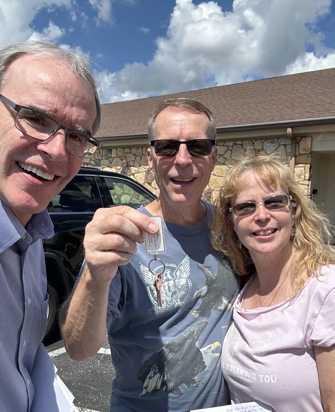 David Campbell, realtor, stands next to a couple composed of Rick and Natasha. Rick is holding up a pair of house keys.