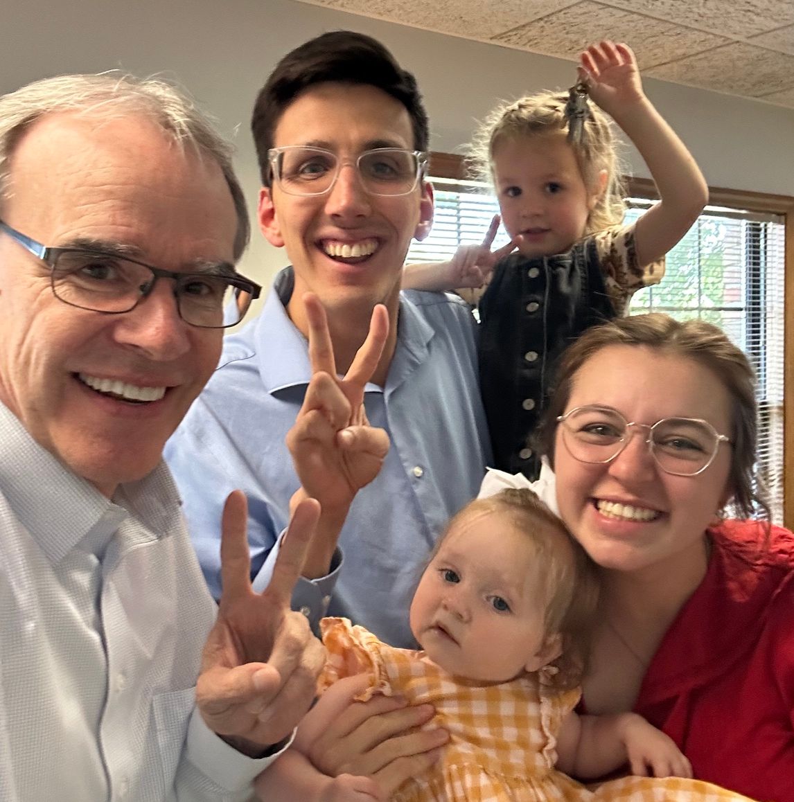 David Campbell, realtor, stands next to both Tim and Julianna as they hold their two daughters up to the camera. One daughter being held by Tim is holding house keys. All but one holds up two fingers, denoting their second sale.