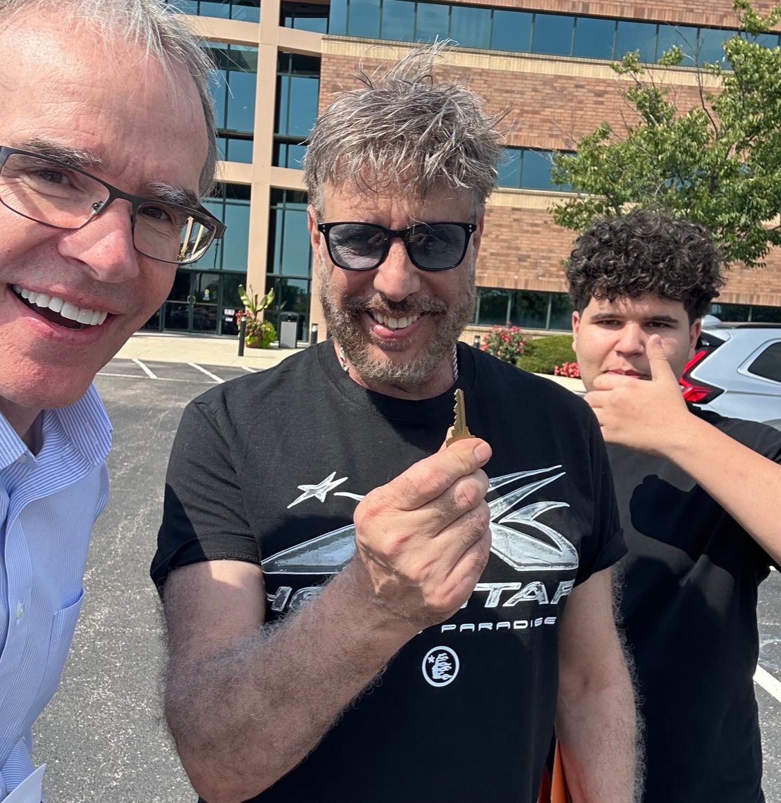 David Campbell, realtor stands with Ramzi and his son as they all face towards the camera, smiling. Ramzi is holding a house key.