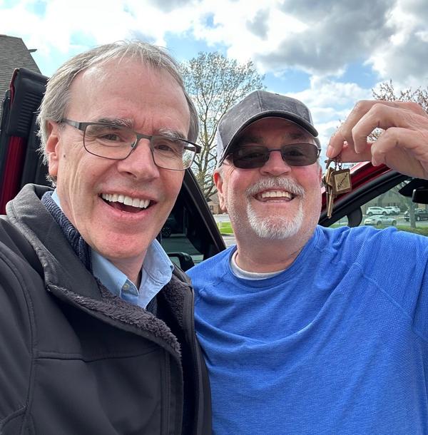 Dave stands next to a man who's holding up keys while they both smile towards the camera.