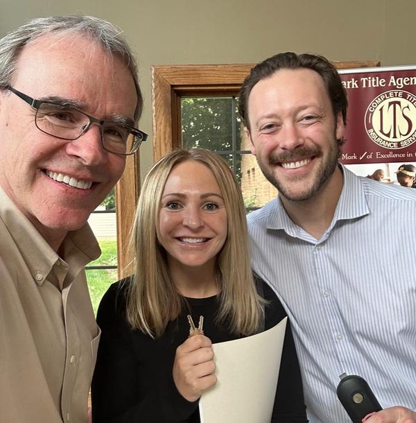 David Campbell, Realtor stands next to a man and woman. The woman is holding two house keys. They're all facing towards the camera, smiling.