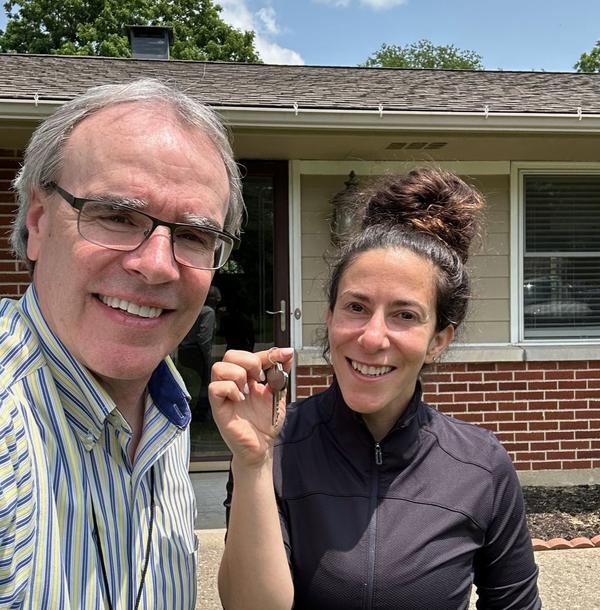 David Campbell, Realtor stands next to a woman holding a house key - they're both facing toward the camera, smiling.