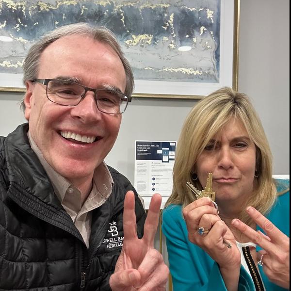David Campbell, Realtor sits next to a woman holding two house keys. They're both facing towards the camera, smiling.