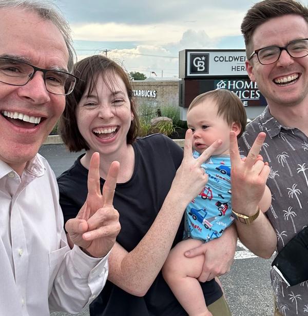 David Campbell, Realtor stands next to a man and women - they're all smiling towards the camera while holding up two fingers. The woman is holding a baby.