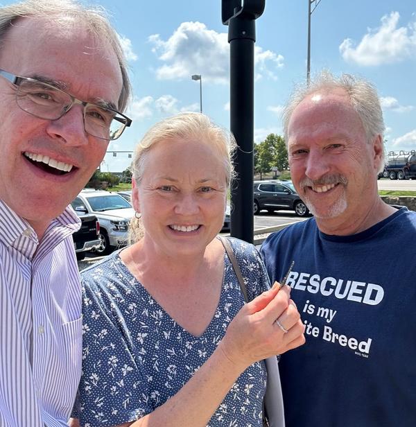 David Cambpell, realtor, stands next to a man and woman - Rob and Dana - as they all face towards the camera, smiling. The woman is holding a house key in her right hand.