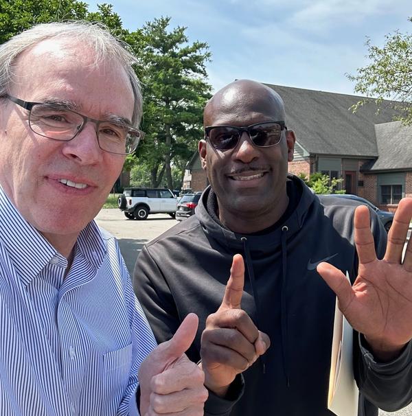 David Campbell, realtor, stands next to a man, Chad, wearing sun glasses as they both face the camera smiling. Chad is holding up six fingers while Dave is giving a thumbs up.