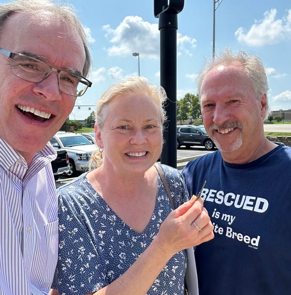 David Cambpell, realtor, stands next to a man and woman as they all face towards the camera, smiling. The woman is holding a house key in her right hand.