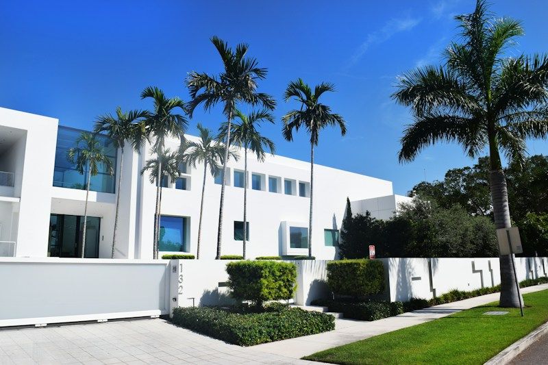 Modern two-story white stucco house behind royal palms in South Florida