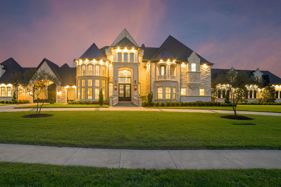 Modern San Antonio luxury home exterior at twilight, showcasing illuminated windows, stone facade, and landscaped front yard.