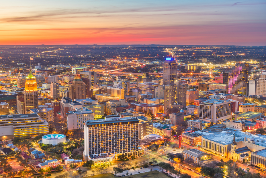 Aerial view of the San Antonio Texas skyline at twilight, featuring downtown buildings, the Tower of the Americas, and illuminated city lights.