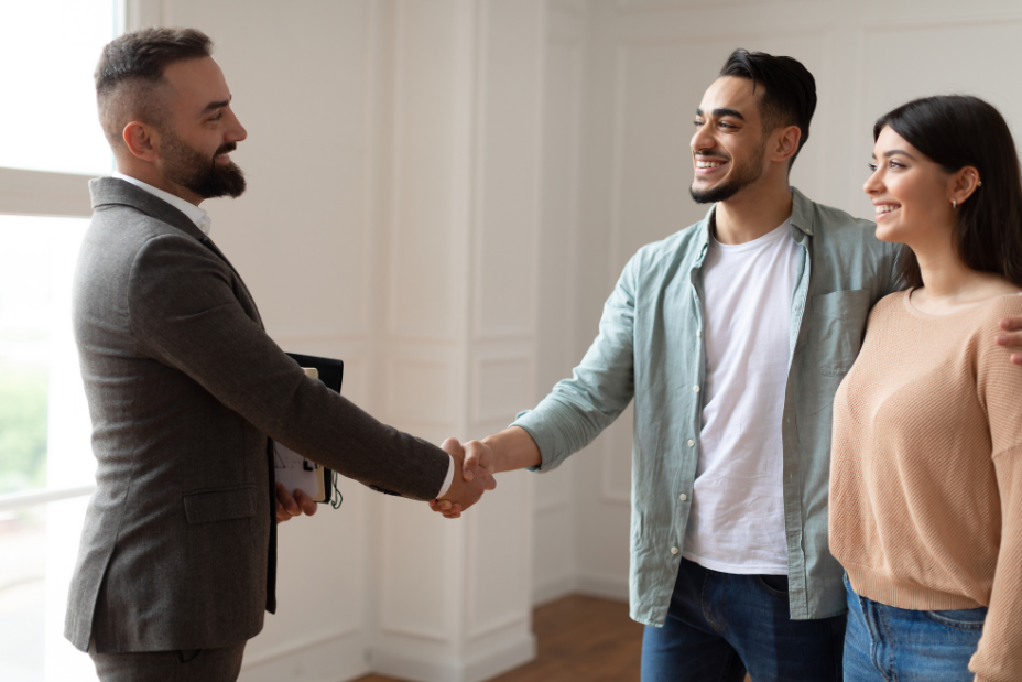 Happy couple shaking hands with a professional real estate agent in a bright room after a successful home purchase.