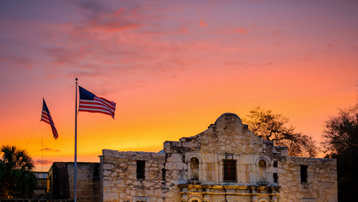Historic Alamo Mission in San Antonio with two American flags flying at sunset