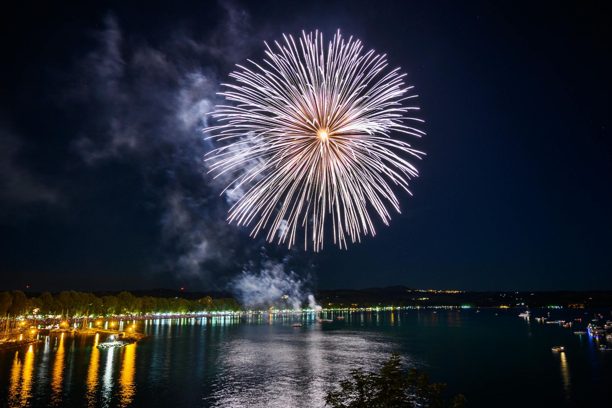 Bright fireworks bursting over a lake at night with colorful reflections on the water
