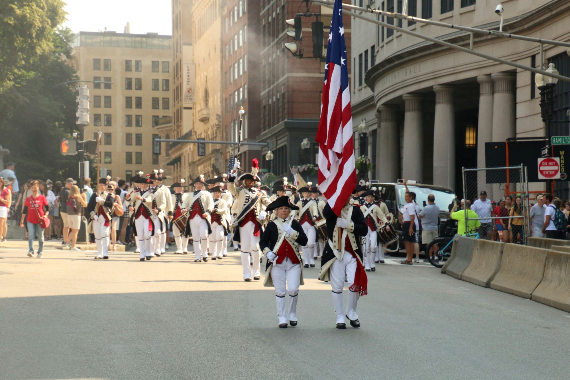Patriotic parade on a city street flanked by tall buildings and rows of American flags