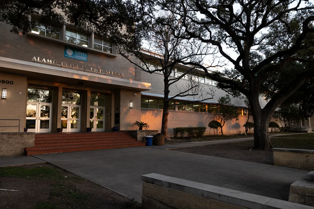 Exterior view of Alamo Heights High School, featuring the main entrance, steps, and trees surrounding the building in the evening light.