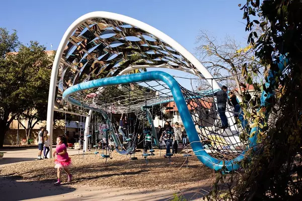 A child joyfully plays on a blue playground structure, climbing and exploring the various features