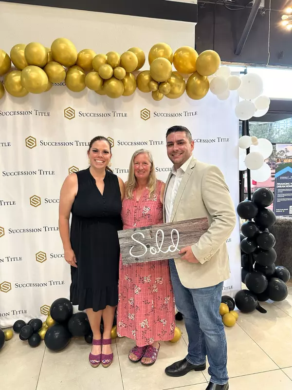 Closing day celebration with a client holding a ‘Sold’ sign in front of the Succession Title backdrop, with balloons and a ‘Sold’ plaque