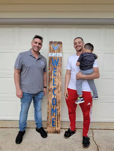 Anthony Sharp delivers a custom ‘Welcome’ porch sign to a new homeowner holding his toddler outside their Cibolo garage