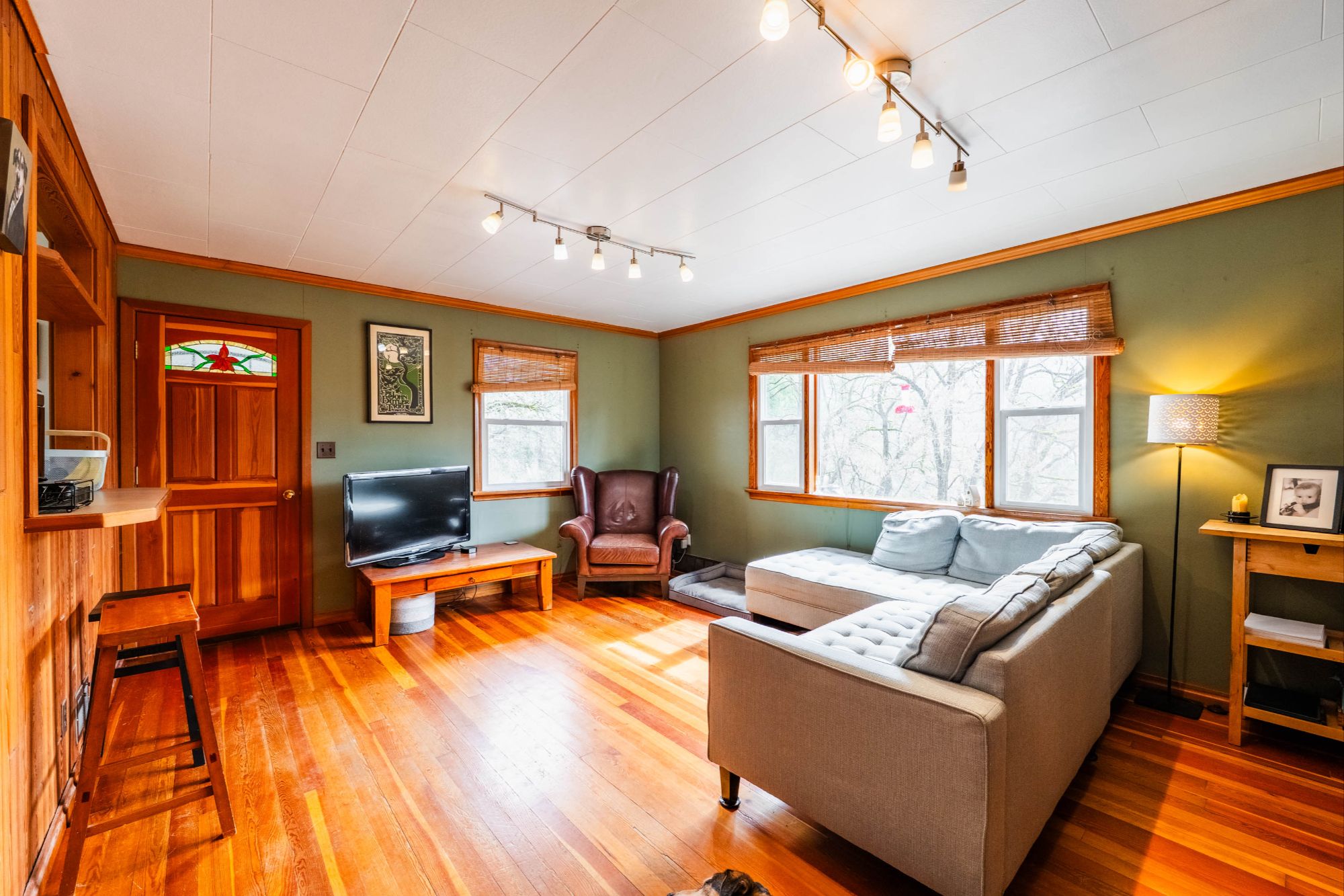 Cozy living room at 3250 South Slocan Village Road featuring hardwood floors, a sectional sofa, wood-trimmed windows, green walls, and a wood stove creating a warm and inviting atmosphere
