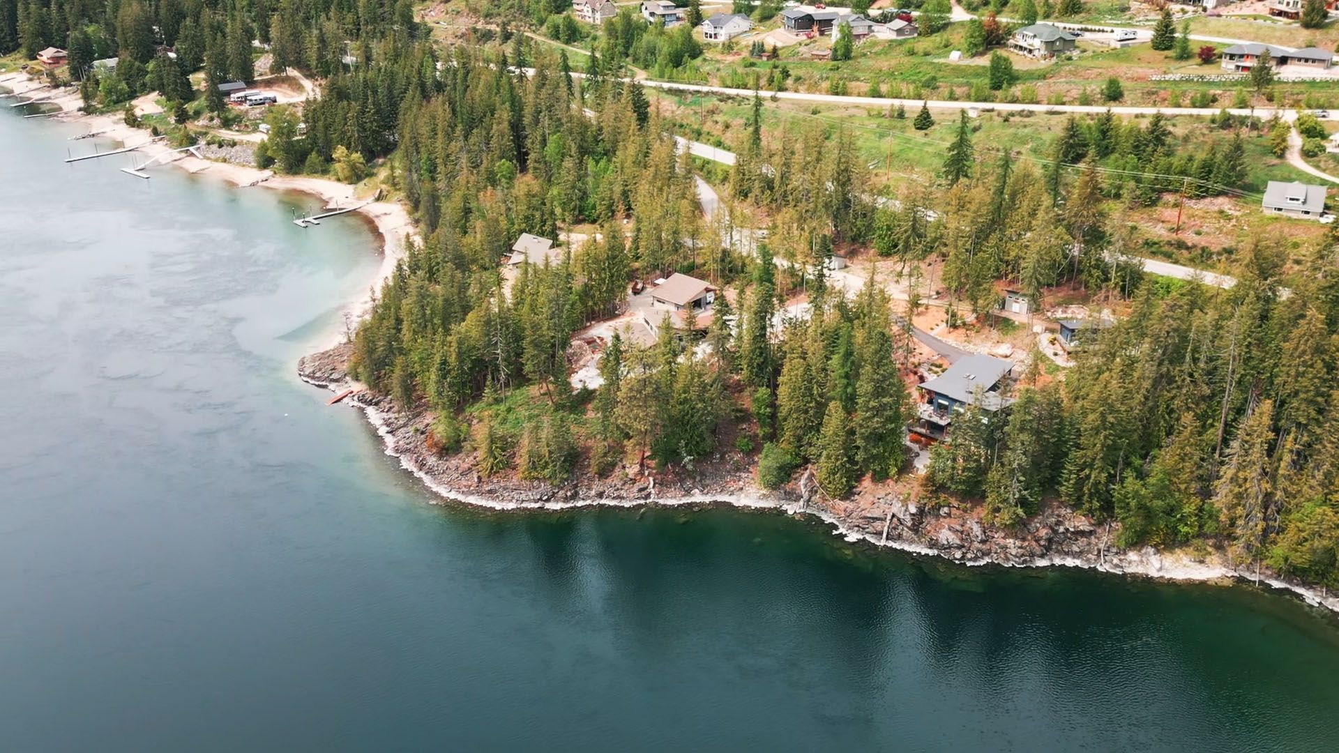 Aerial view of waterfront properties and forested lots along Kootenay Lake near Nelson, BC, showcasing sandy beaches, private docks, and a winding shoreline.
