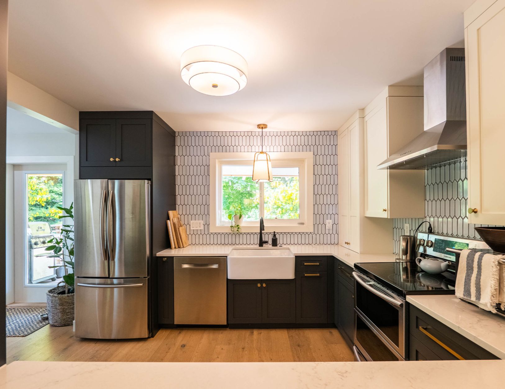 Bright, stylish kitchen featuring a farmhouse sink, stainless steel appliances, two-tone cabinetry, quartz countertops, and unique geometric tile backsplash, with natural light streaming through a large window above the sink.