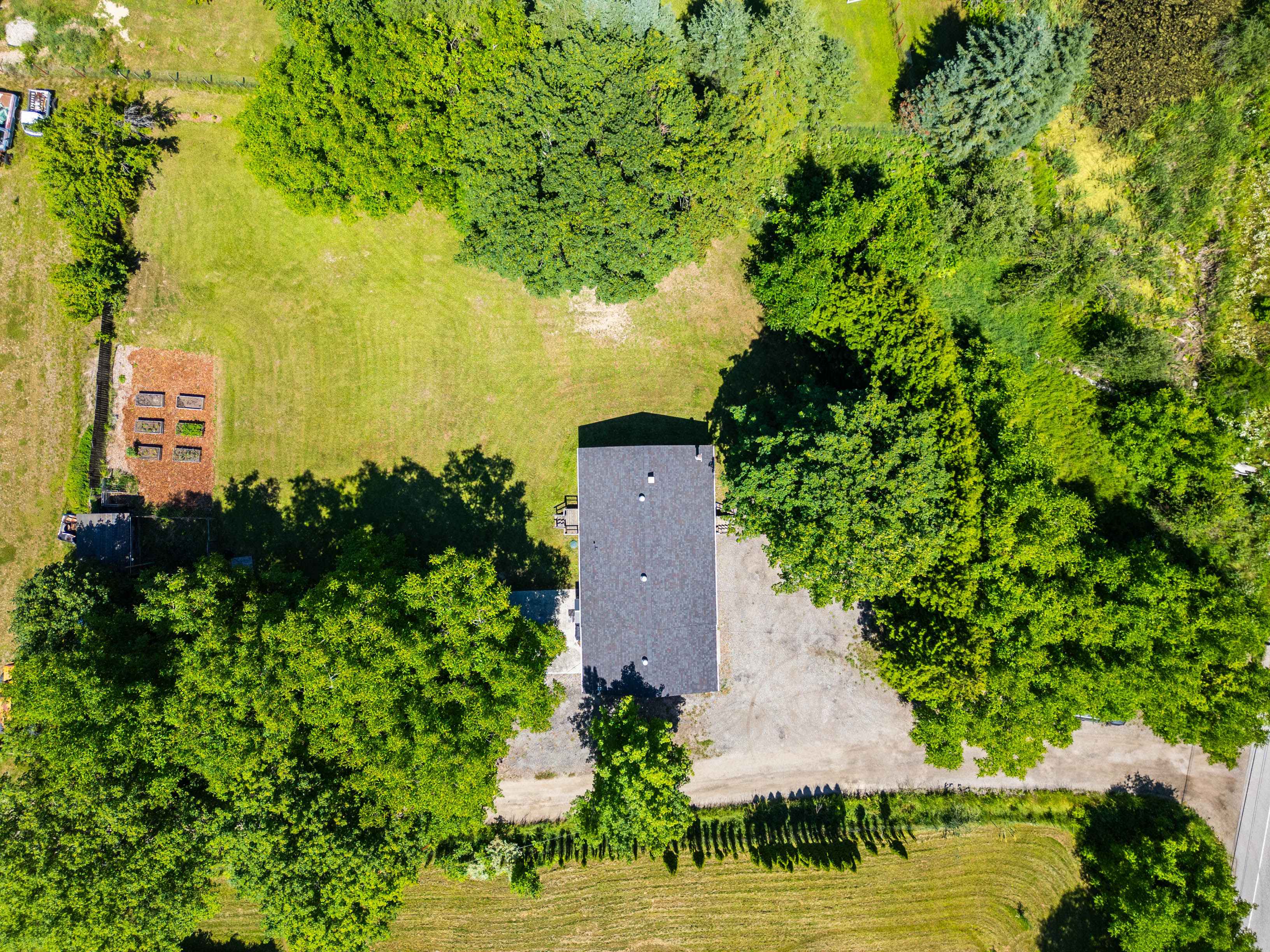 Aerial view of a single-family home on a spacious .84-acre lot in Thrums, BC, surrounded by mature trees and greenery, with a large garden area and open lawn