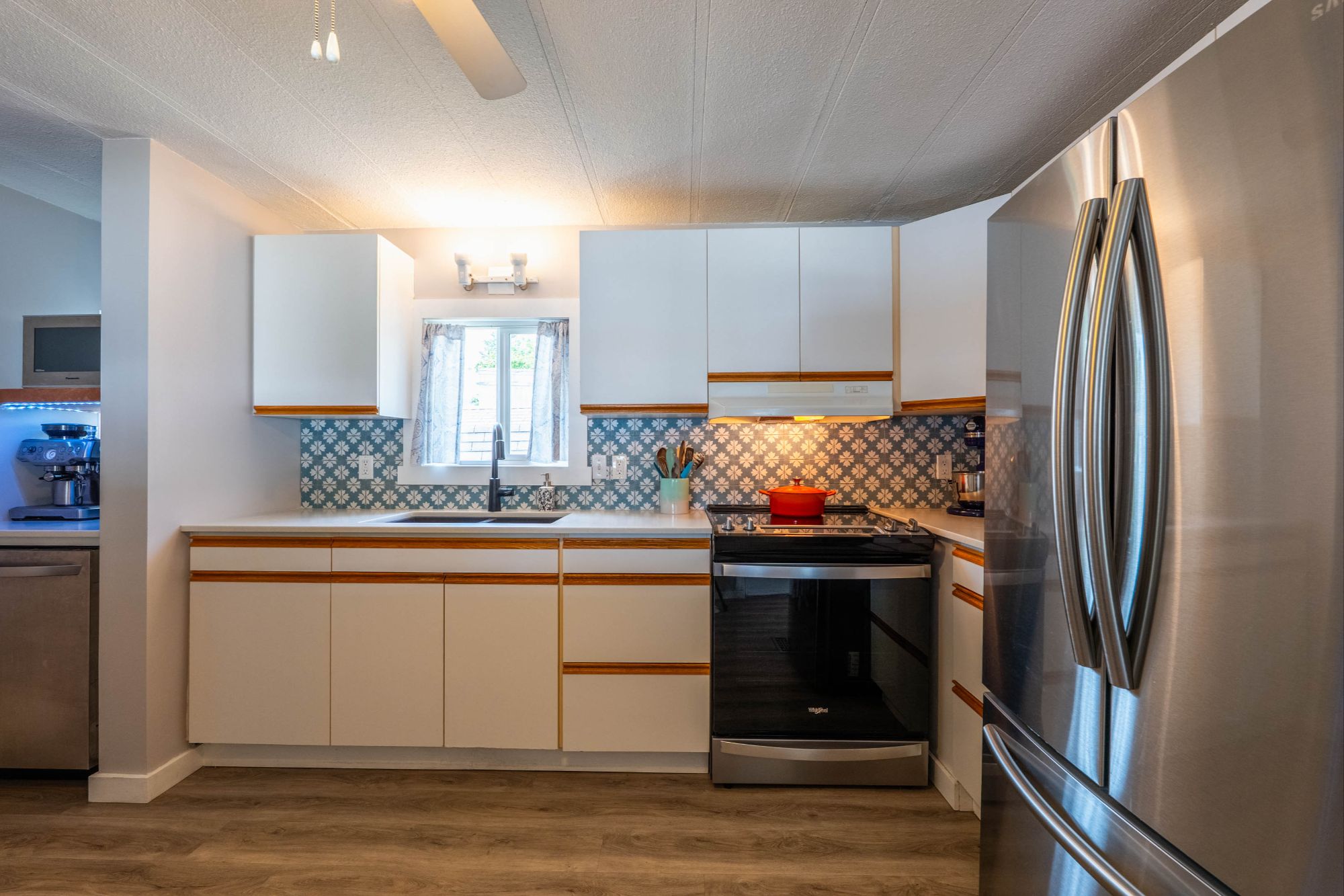 Bright, modern kitchen with stainless steel appliances, white cabinetry, and patterned tile backsplash in a renovated manufactured home near Nelson, BC