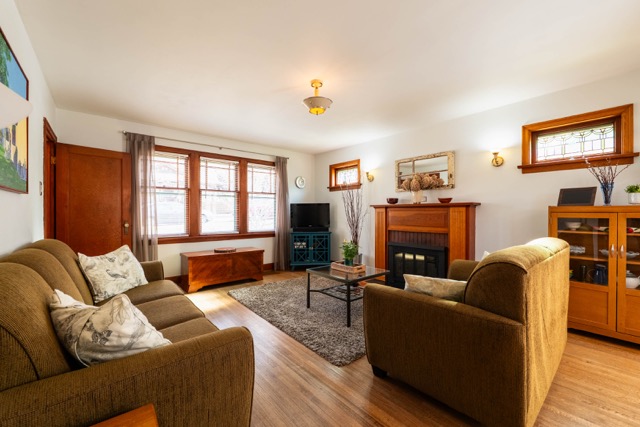 Living room in Nelson BC 1939 heritage home with hardwood floors, wood-trimmed windows, vintage light fixtures, and original fireplace