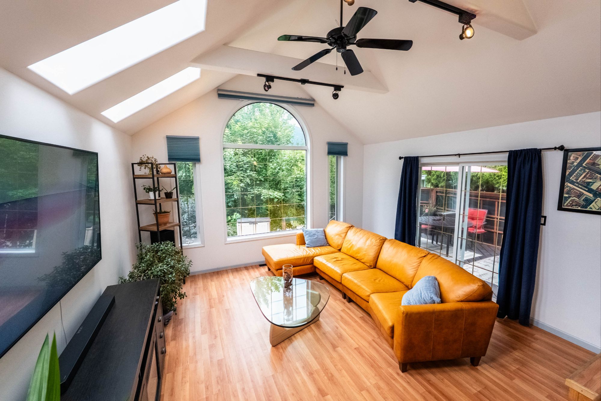 Bright living room with vaulted ceilings, large arched window, skylights, and sliding doors to a private deck in a Nelson BC home