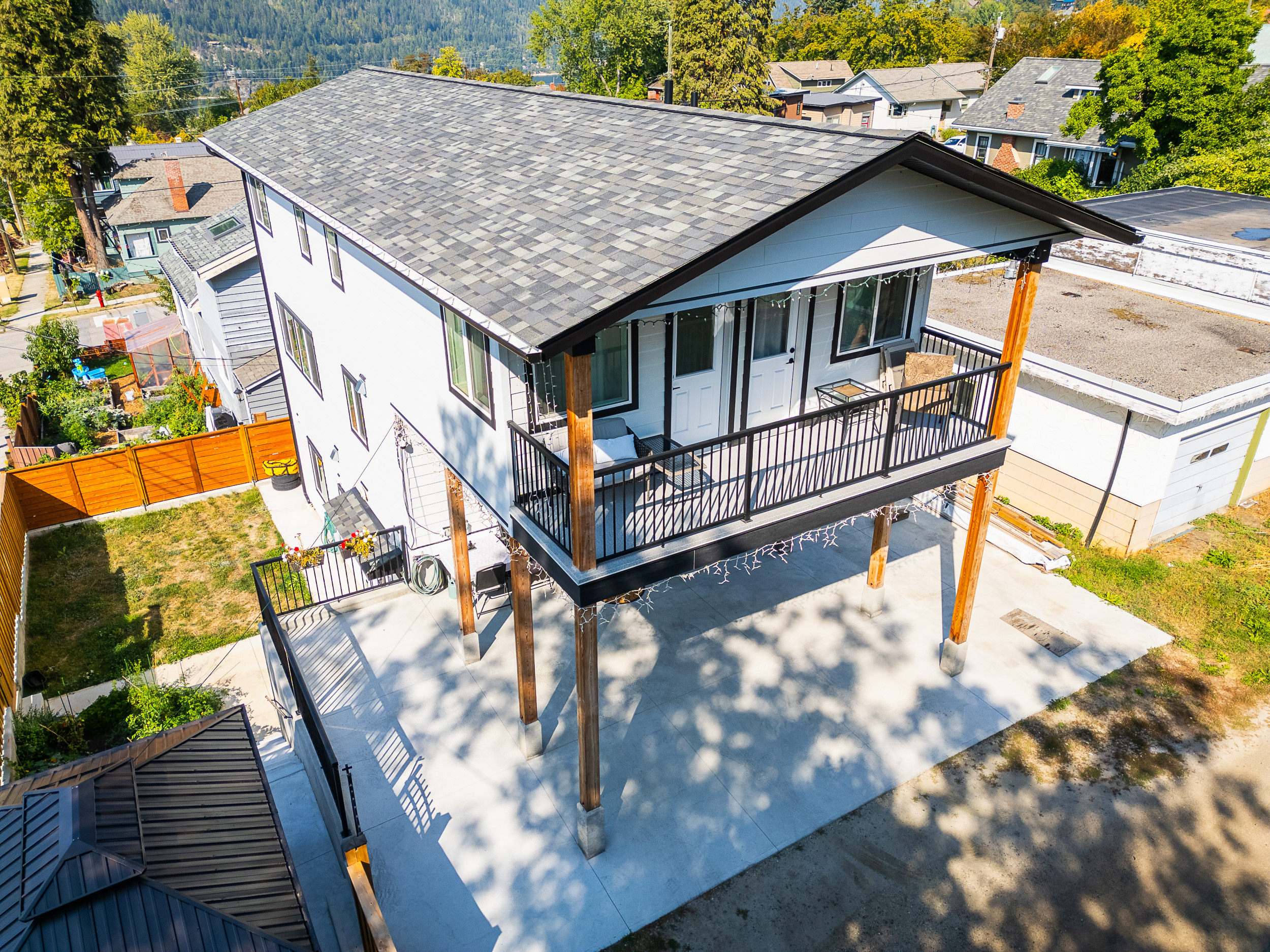 Overhead view of a two-storey modern home in Nelson BC with a covered upper balcony, exposed timber posts, large concrete parking area, and scenic surroundings — ideal for multi-family living or rental investment in the Uphill neighbourhood.