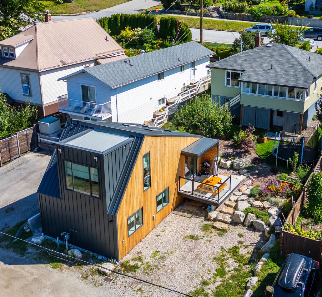 Aerial view of Nelson BC property featuring a modern two-bedroom laneway house with wood and black metal siding, alongside the original character home on a generous double lot in the Uphill neighbourhood