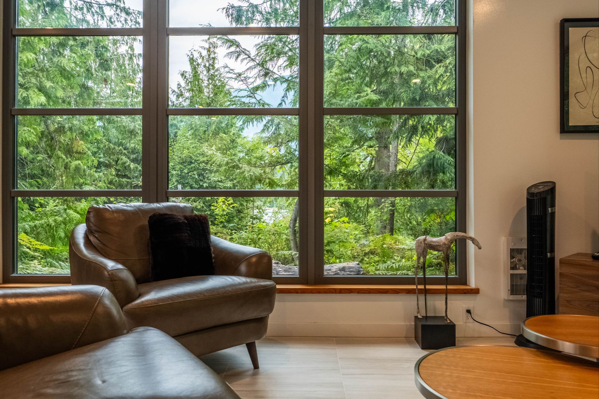 Interior living space at 183–191 Kootenay Lake Road with expansive windows overlooking forested Kootenay Lake surroundings