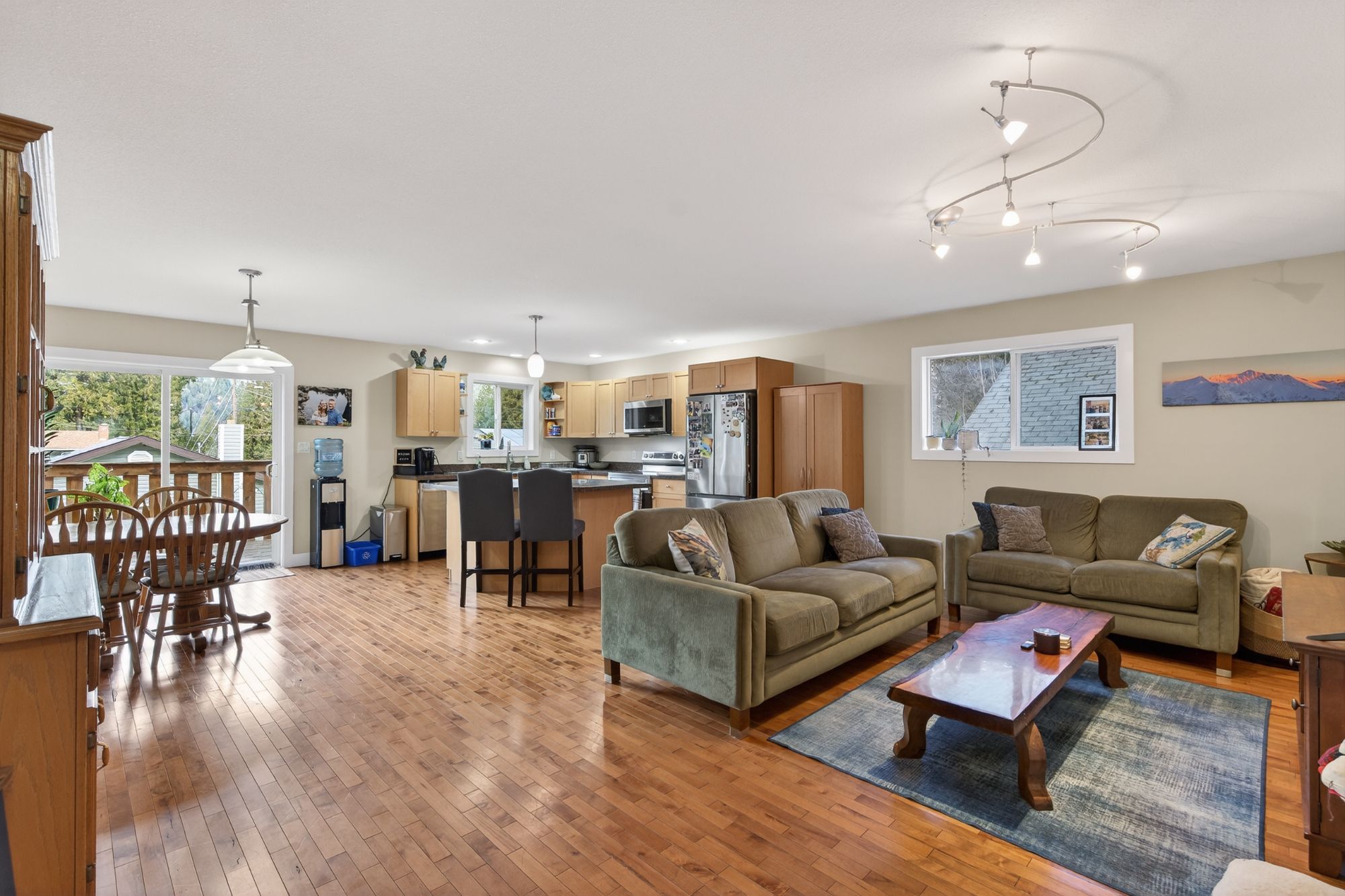 Bright open-concept living room and kitchen with hardwood floors, large windows, and direct access to deck in a Castlegar BC home.