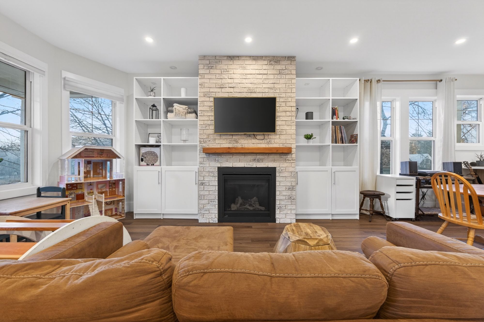 Bright living room with built-in shelving, brick fireplace, mounted TV, and large windows in a renovated heritage home in Nelson BC