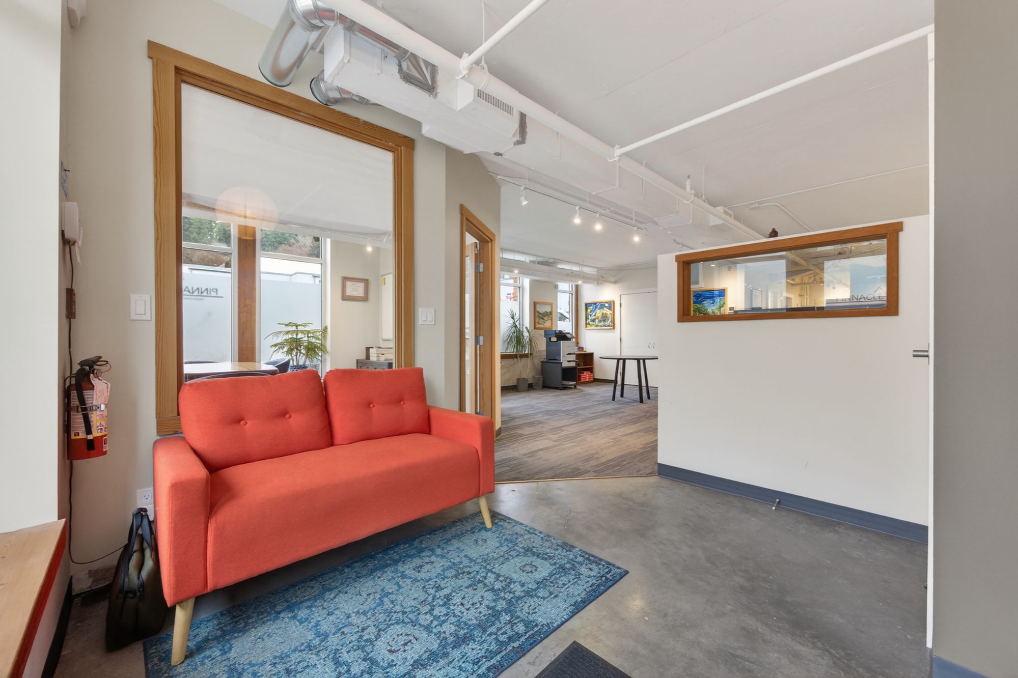 Reception area inside 754 Vernon Street commercial office for sale in downtown Nelson BC featuring red sofa, polished concrete floors, and open-concept workspace.