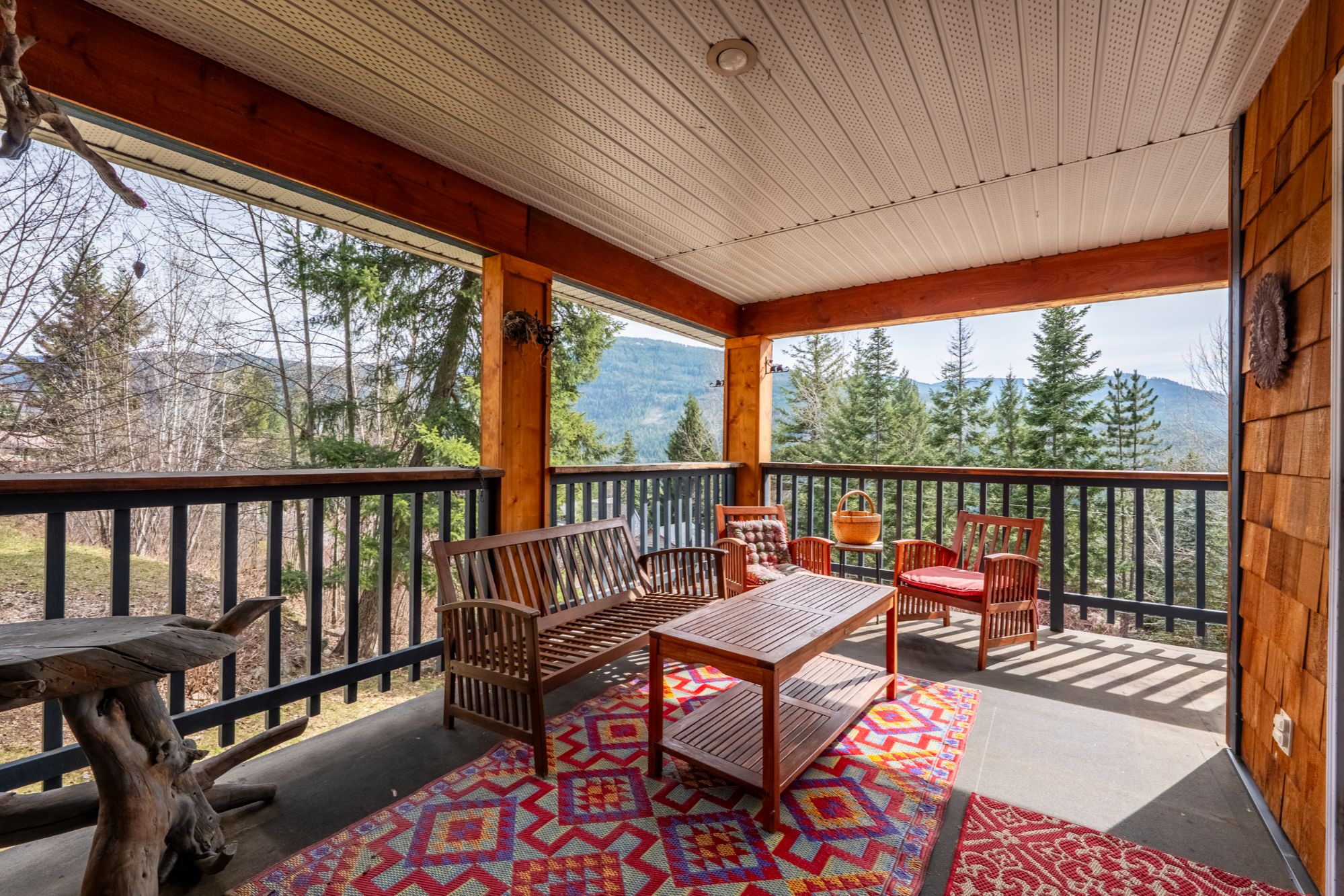 Covered deck with wood beams, outdoor seating, and mountain views at Bonnington home