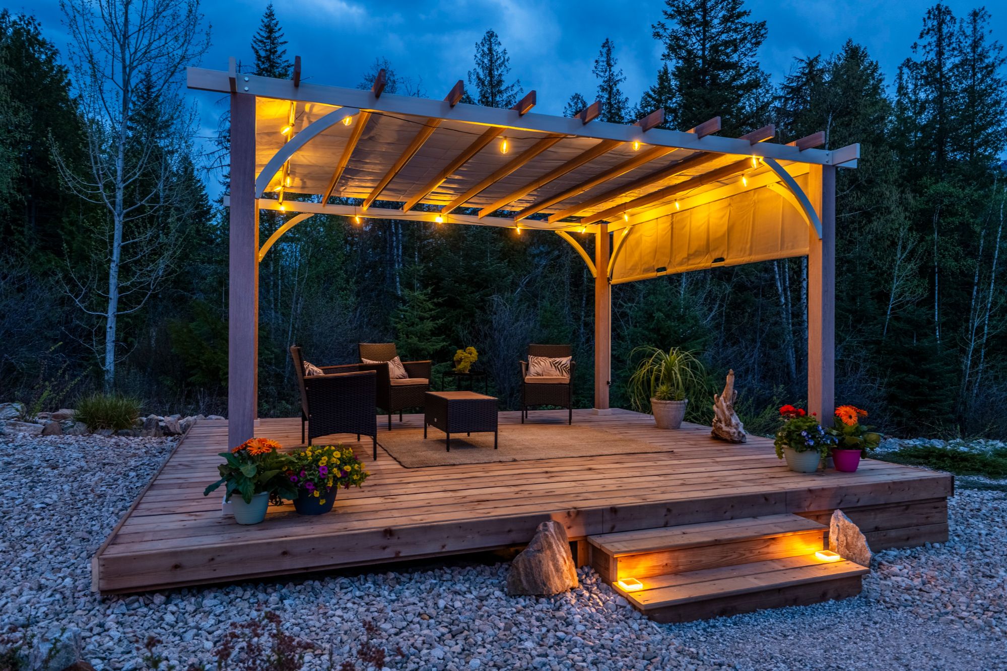 Outdoor pergola lounge at 430 Buriview Drive in Nelson BC, featuring a covered deck with ambient lighting, seating area, and private forest setting for evening relaxation.