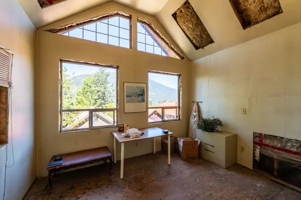 Unfinished upper-level room in a Nelson BC home with vaulted ceiling, exposed insulation, large windows offering mountain views, and minimal furnishings