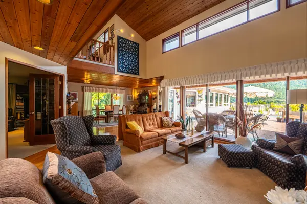 Spacious living room with vaulted wood ceilings, large windows, and patio access at 1896 Hwy 3A, Nelson BC waterfront home – MLS® 10360967