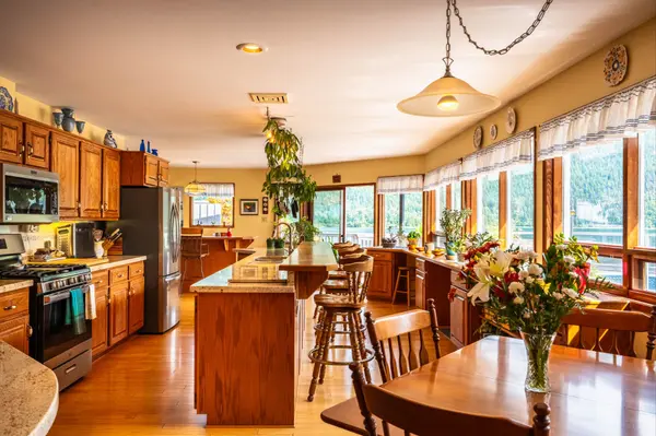Bright kitchen with wood cabinetry, large island, dining area, and expansive lakeview windows at 1896 Hwy 3A, Nelson BC waterfront home – MLS® 10360967.