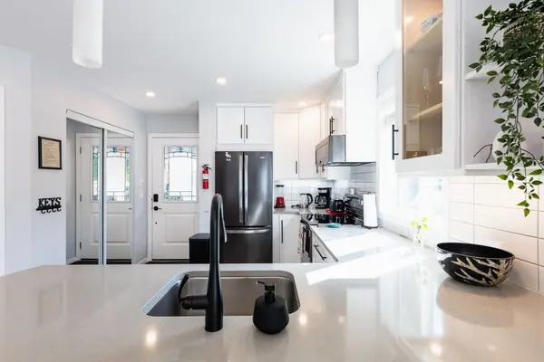 View from the kitchen island of a contemporary Nelson BC home, showcasing sleek quartz countertops, matte black fixtures, stainless steel Whirlpool appliances, and white shaker cabinets with modern hardware, positioned near a stylish entryway with frosted glass doors and ample natural light.