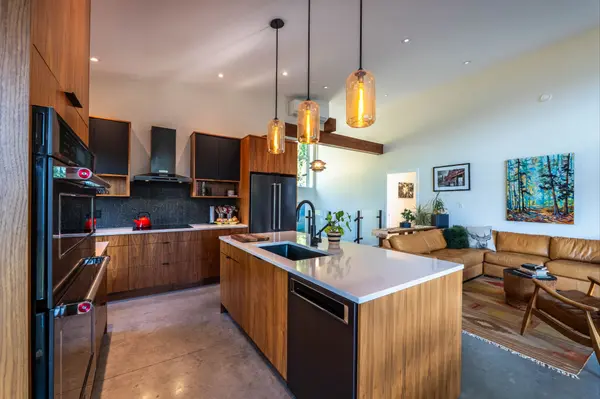 Modern open-concept kitchen and living area featuring custom Spruced Kitchens cabinetry, quartz island, designer lighting, and polished concrete floors at 1409 Ash Street in Nelson, BC