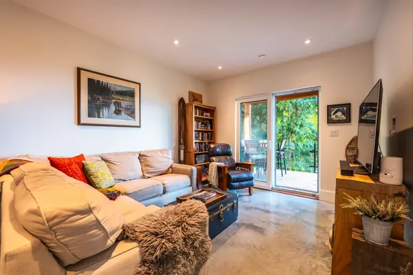 Comfortable media room with sectional sofa, reading nook, and sliding glass doors leading to a private deck surrounded by trees at 1409 Ash Street, Nelson BC