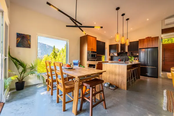 Bright dining area with mountain views, adjacent to a custom modern kitchen with wood cabinetry, pendant lighting, and polished concrete floors at 1409 Ash Street, Nelson BC