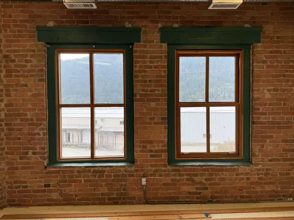 “Large double windows with green trim in Nelson’s historic Cornerbrick Building, showcasing exposed brick walls and mountain views—bright natural light ideal for office or retail use.