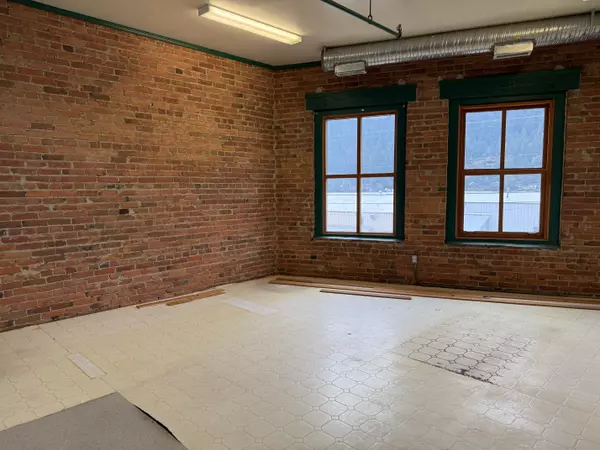 “Second-floor commercial space in Nelson’s CorConerbrick Building with exposed brick walls, large windows framing mountain views, and bright natural light—ideal for retail or office use.