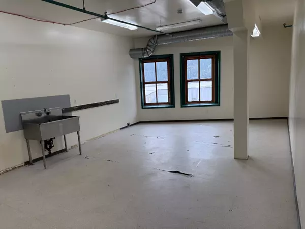 Spacious commercial unit in Nelson’s Cornerbrick Building featuring large windows with mountain views, bright natural light, white walls, exposed ductwork, and utility sink—versatile space for retail or office use.