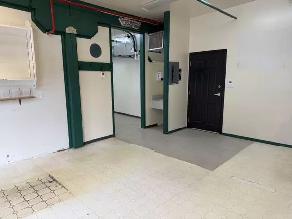 Interior view of commercial unit in Nelson’s Cornerbrick Building, featuring tiled flooring, black door entry, open wall shelving, and green-trimmed support beams—versatile space for retail or office use.
